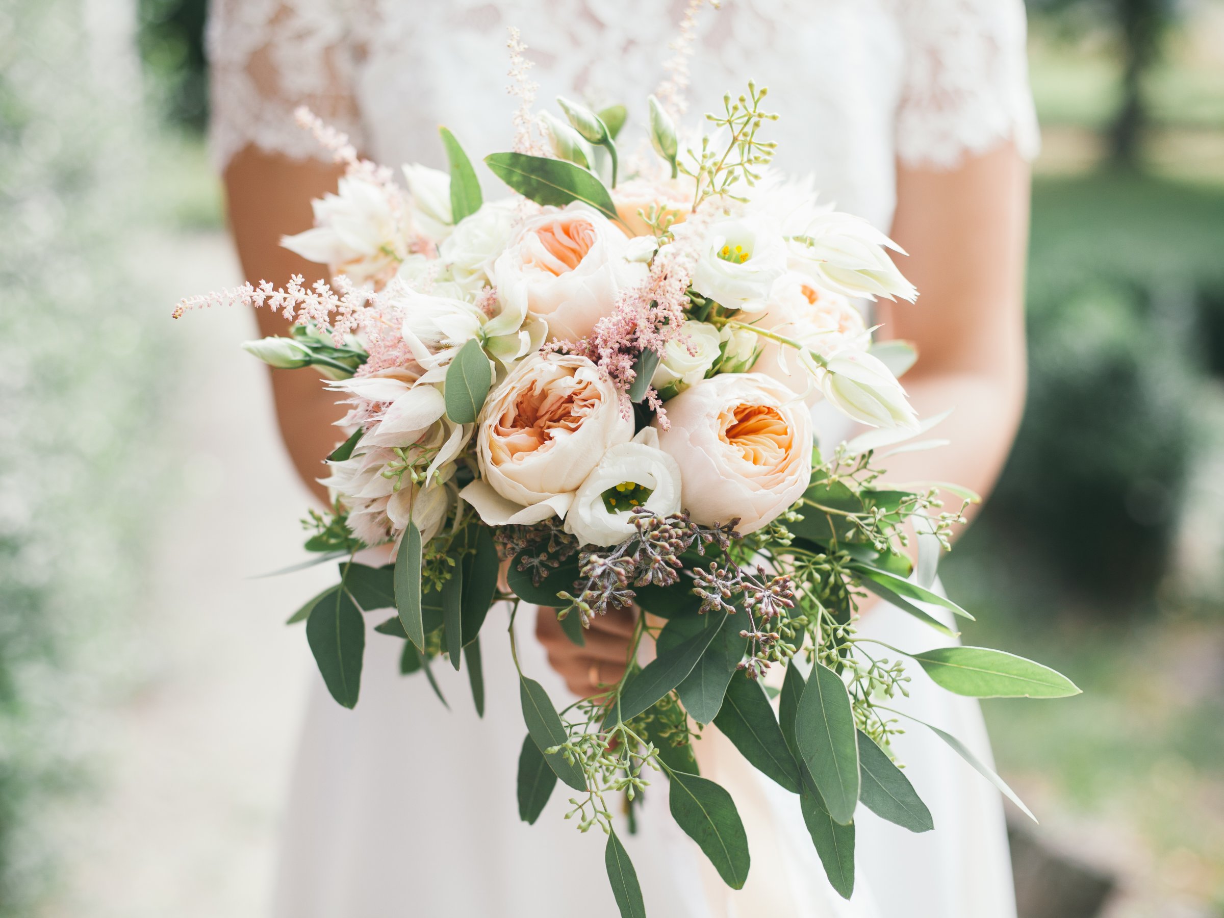 A bride holding a bouquet of pale roses and eucalyptus